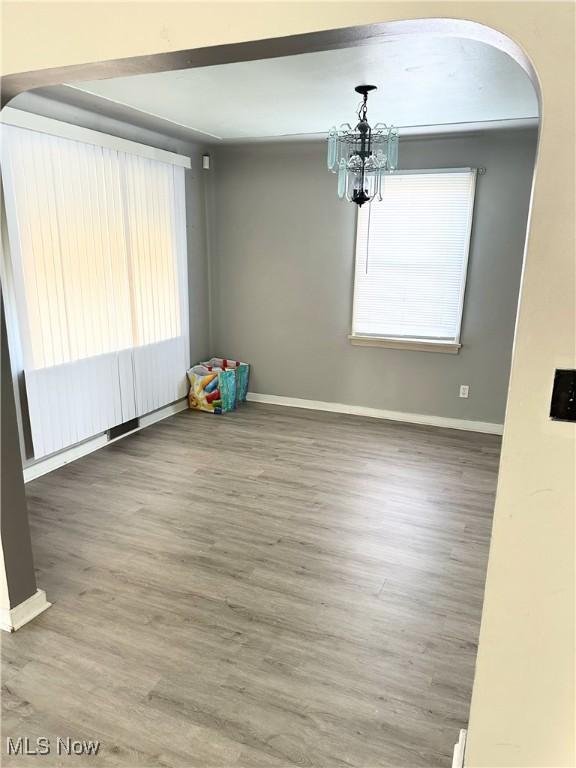 unfurnished room featuring arched walkways, a notable chandelier, wood finished floors, and baseboards