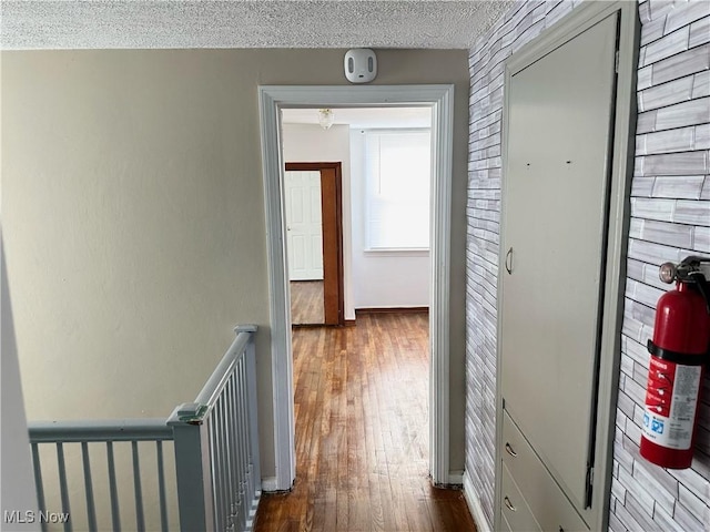 hall with a textured ceiling, dark wood-style flooring, and baseboards