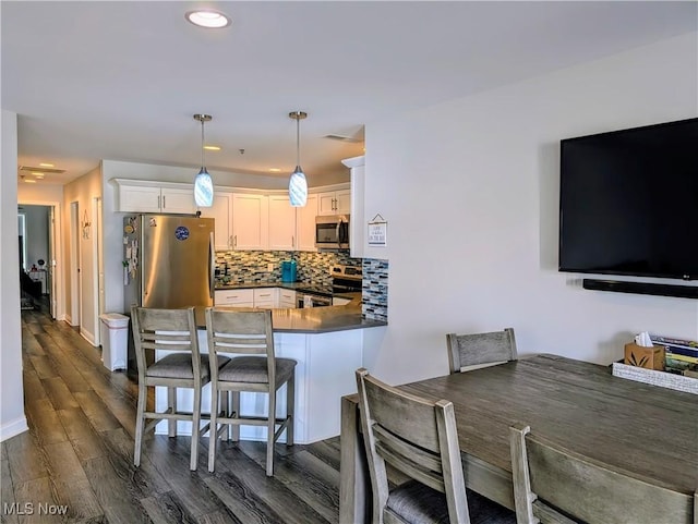 kitchen featuring dark wood finished floors, decorative backsplash, dark countertops, a peninsula, and stainless steel appliances