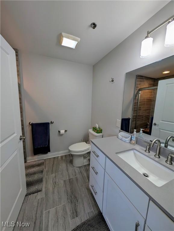 full bath featuring toilet, vanity, a shower stall, wood finished floors, and baseboards