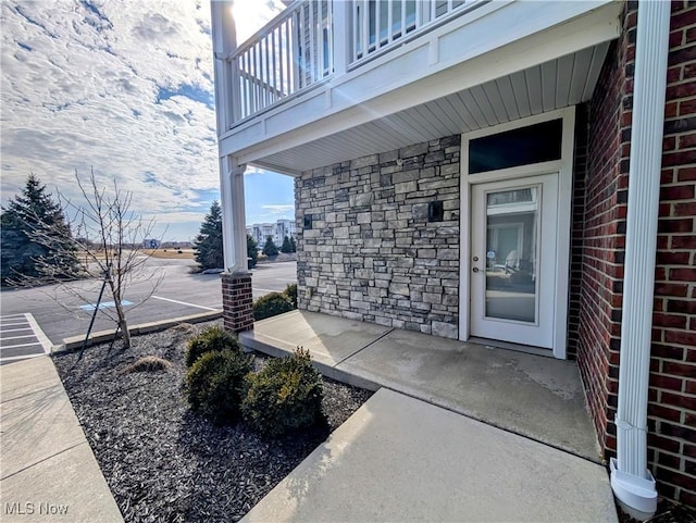 entrance to property featuring a balcony, stone siding, covered porch, and brick siding