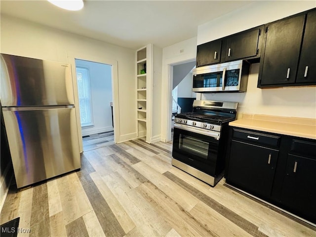 kitchen featuring light wood-style floors, stainless steel appliances, dark cabinets, and light countertops