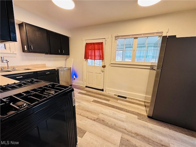 kitchen featuring black range with gas cooktop, freestanding refrigerator, dark cabinetry, light wood-style floors, and a sink