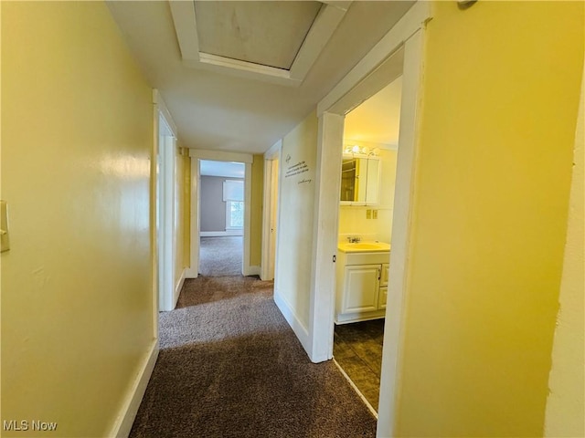 hallway with a sink, baseboards, dark carpet, and attic access