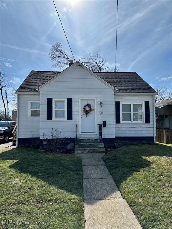 bungalow-style home with a front yard, roof with shingles, and fence