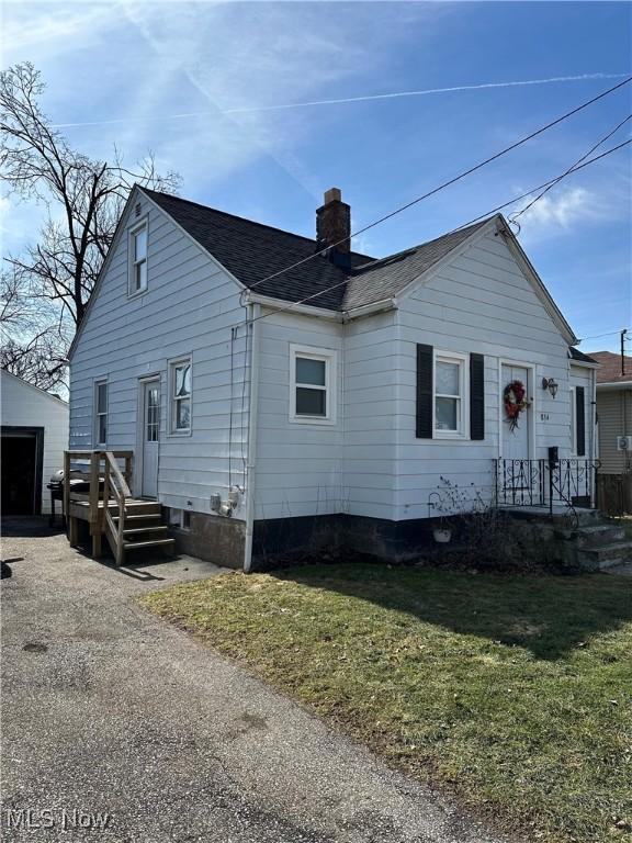 exterior space with a front yard, roof with shingles, a chimney, and an outbuilding