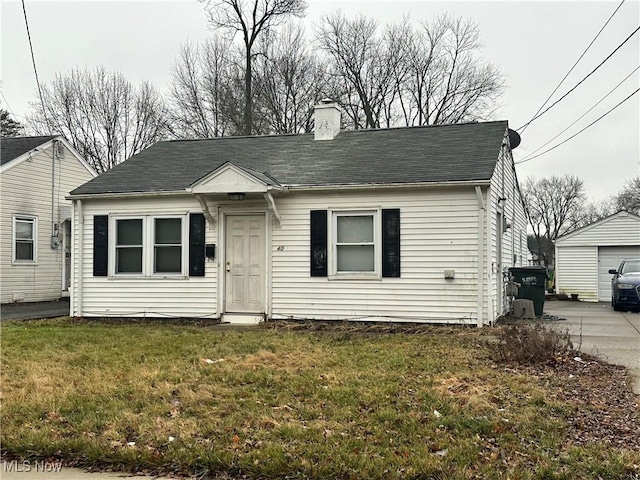 bungalow-style house featuring a front yard, roof with shingles, a chimney, and an outdoor structure