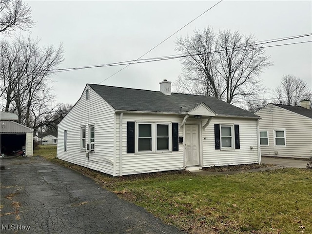 bungalow with a chimney, a front lawn, a detached garage, and an outbuilding