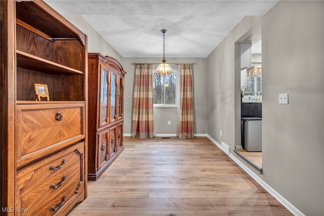 dining room featuring light wood-type flooring, baseboards, and a textured ceiling