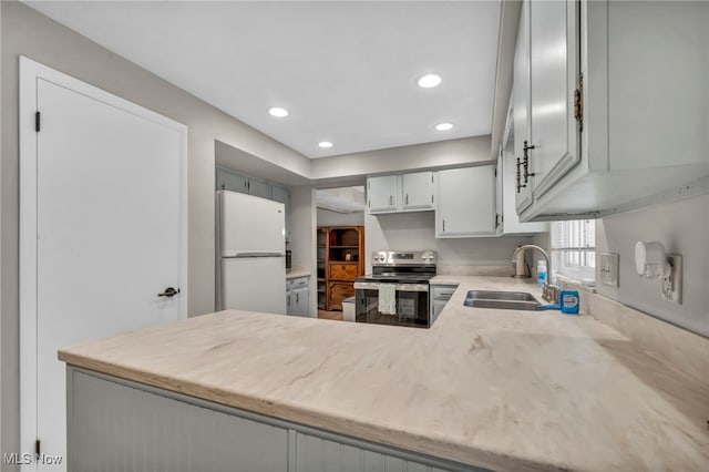 kitchen featuring stainless steel electric stove, light countertops, freestanding refrigerator, a sink, and a peninsula