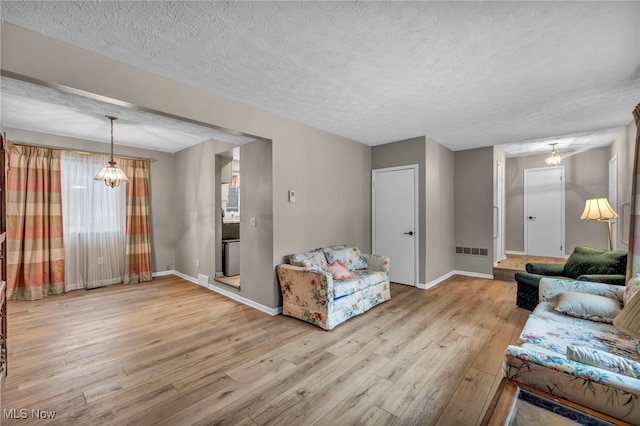 living area with a textured ceiling, a chandelier, visible vents, baseboards, and light wood finished floors