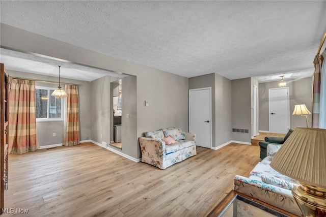 living area featuring light wood-type flooring, visible vents, baseboards, and a textured ceiling