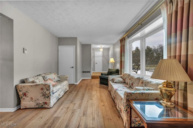 living room with light wood finished floors, visible vents, baseboards, and a textured ceiling