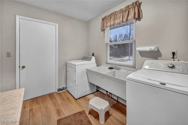 washroom with light wood-style floors, a sink, a textured ceiling, separate washer and dryer, and laundry area