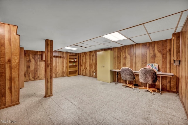 finished basement featuring wood walls, built in study area, a drop ceiling, and tile patterned floors