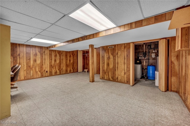 finished basement with baseboards, a drop ceiling, wooden walls, and light floors