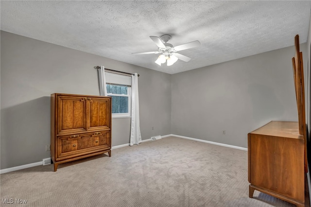 unfurnished bedroom featuring a ceiling fan, light colored carpet, a textured ceiling, and baseboards