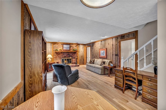 living area featuring light wood-style floors, stairway, a fireplace, and a textured ceiling