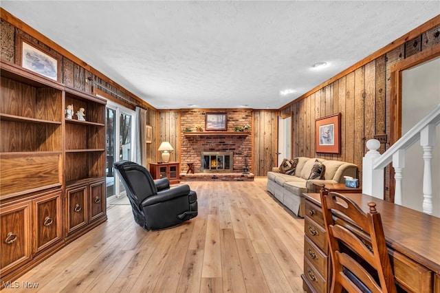 living room featuring a brick fireplace, light wood-style flooring, stairway, and a textured ceiling