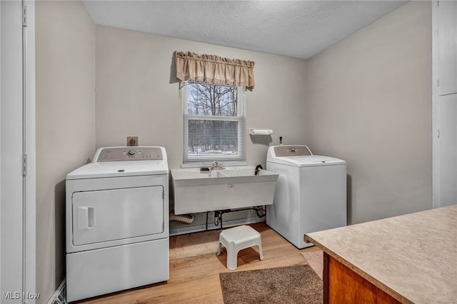 washroom with a textured ceiling, light wood-style flooring, laundry area, a sink, and washer and dryer