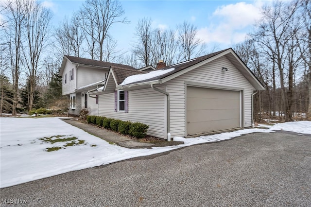 view of snow covered exterior featuring a garage, a chimney, and aphalt driveway