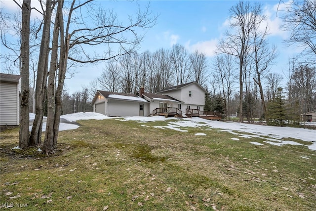 view of snow covered exterior with an attached garage, a chimney, a lawn, and a wooden deck