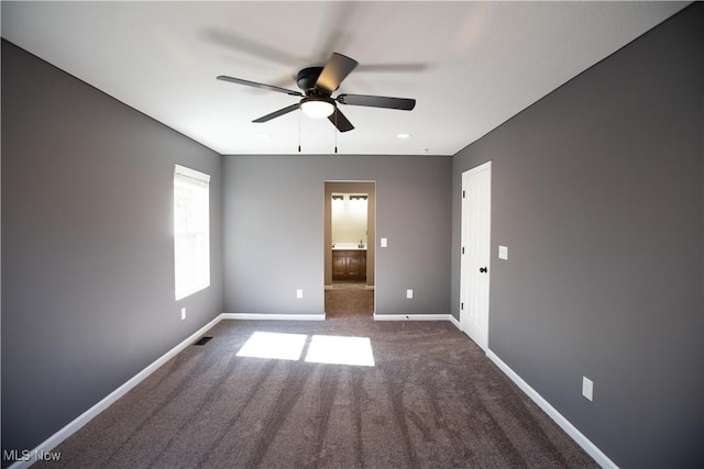 spare room featuring baseboards, dark carpet, and a ceiling fan