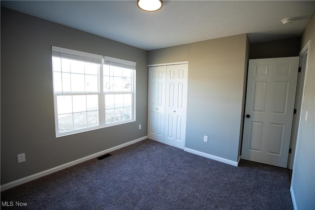 unfurnished bedroom with a closet, dark carpet, visible vents, and baseboards