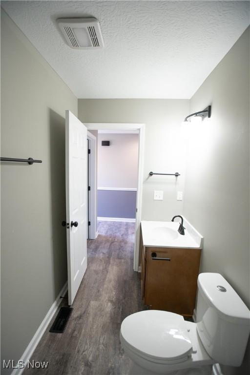 half bathroom featuring toilet, a textured ceiling, vanity, and visible vents