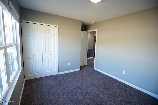 unfurnished bedroom with a closet, multiple windows, dark carpet, and baseboards