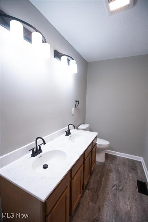 bathroom featuring toilet, double vanity, a sink, and wood finished floors