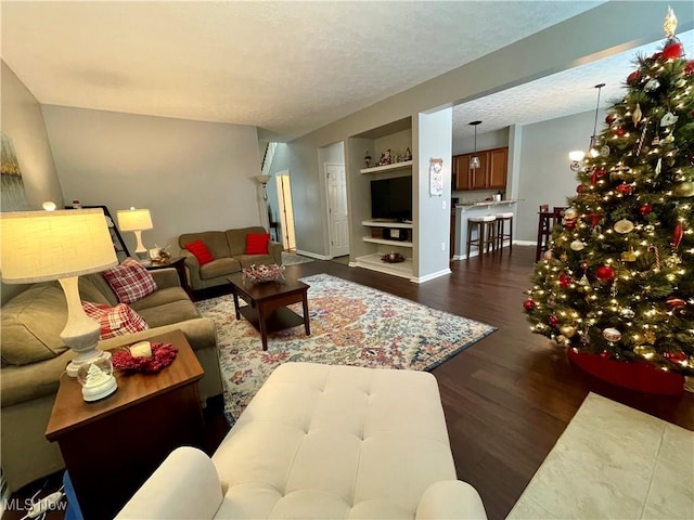 living room featuring a textured ceiling, a chandelier, baseboards, built in features, and dark wood finished floors