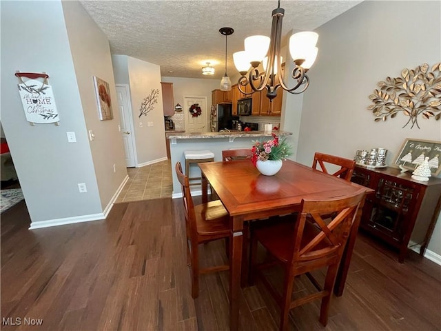 dining area featuring a chandelier, dark wood-style flooring, a textured ceiling, and baseboards