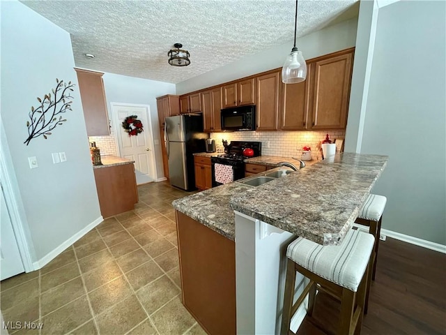 kitchen with brown cabinets, a breakfast bar, a sink, black appliances, and backsplash