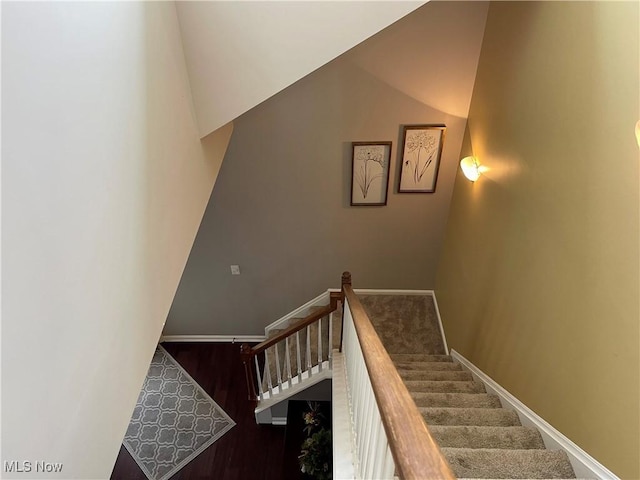 stairway featuring lofted ceiling, baseboards, and wood finished floors