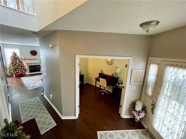 foyer entrance featuring a fireplace with flush hearth, baseboards, and wood finished floors