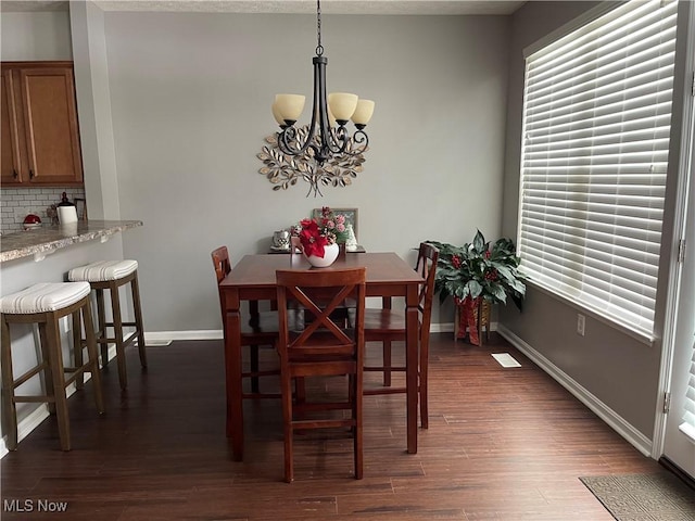 dining area with dark wood-type flooring, a notable chandelier, and baseboards