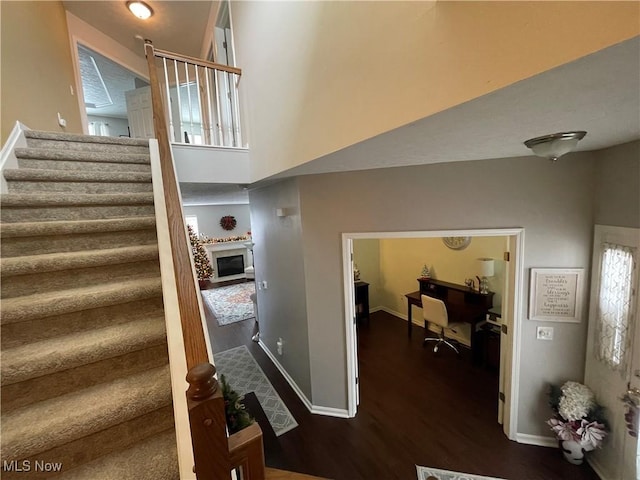 staircase featuring a towering ceiling, a fireplace, baseboards, and wood finished floors