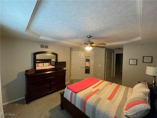 bedroom with a raised ceiling, light colored carpet, visible vents, a ceiling fan, and a textured ceiling