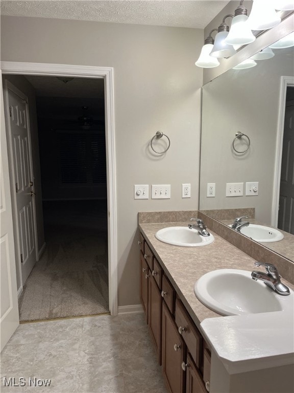 full bath with double vanity, a textured ceiling, and a sink