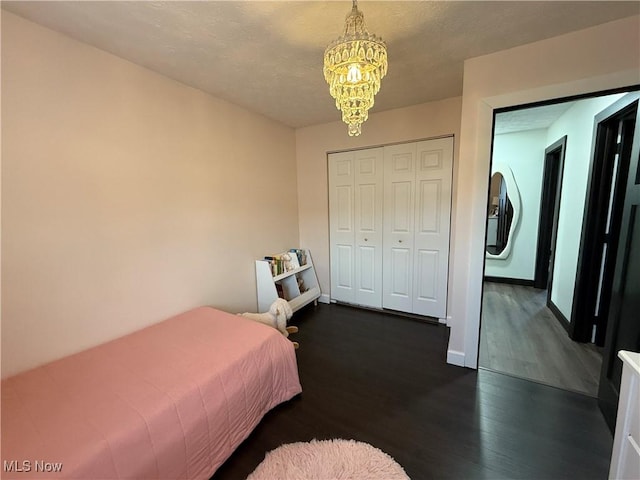 bedroom with a closet, dark wood-style flooring, baseboards, and an inviting chandelier