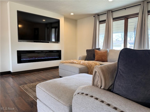 living area with a glass covered fireplace, baseboards, hardwood / wood-style floors, and recessed lighting