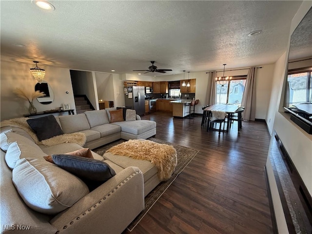 living area featuring a textured ceiling, ceiling fan with notable chandelier, dark wood-style flooring, baseboards, and stairway