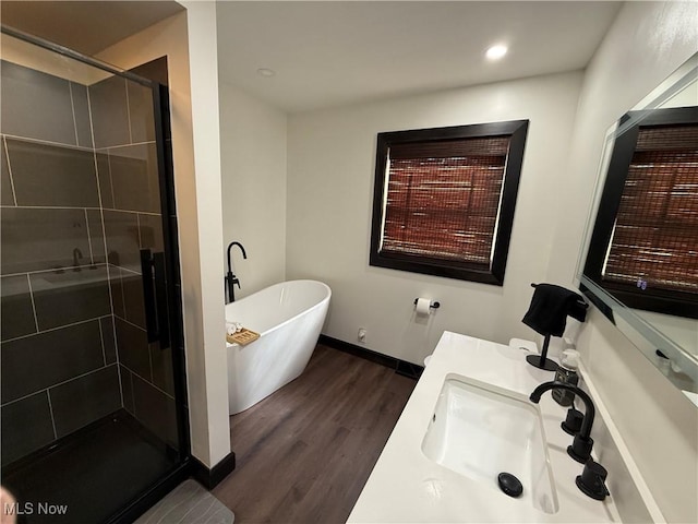 bathroom with a stall shower, baseboards, wood finished floors, a freestanding bath, and vanity