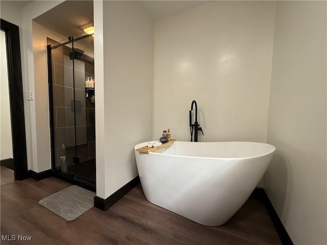 bathroom featuring a stall shower, a freestanding tub, baseboards, and wood finished floors