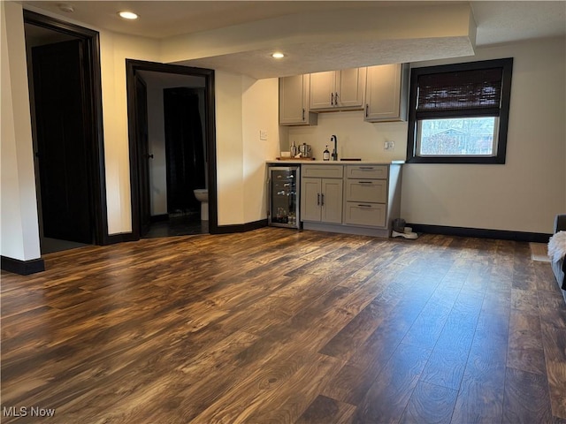 bar featuring beverage cooler, dark wood-style flooring, a sink, baseboards, and wet bar