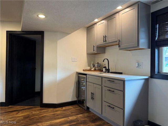 kitchen with wine cooler, dark wood-style flooring, light countertops, gray cabinetry, and a textured ceiling