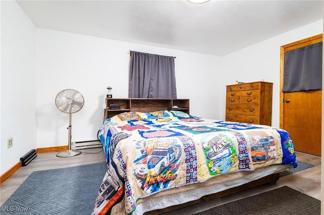 bedroom featuring a baseboard radiator, baseboards, and wood finished floors