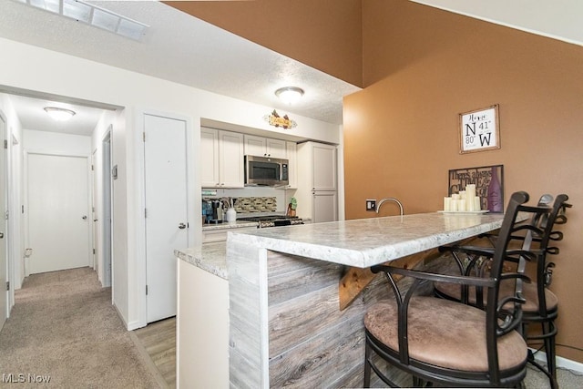 kitchen featuring light carpet, baseboards, visible vents, stainless steel microwave, and light stone countertops