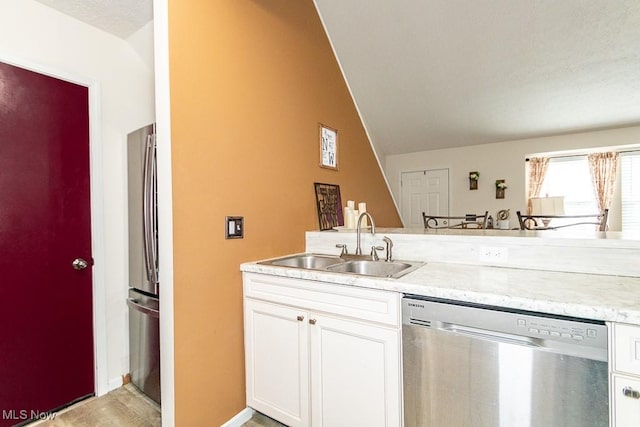 kitchen featuring appliances with stainless steel finishes, white cabinets, vaulted ceiling, a sink, and baseboards